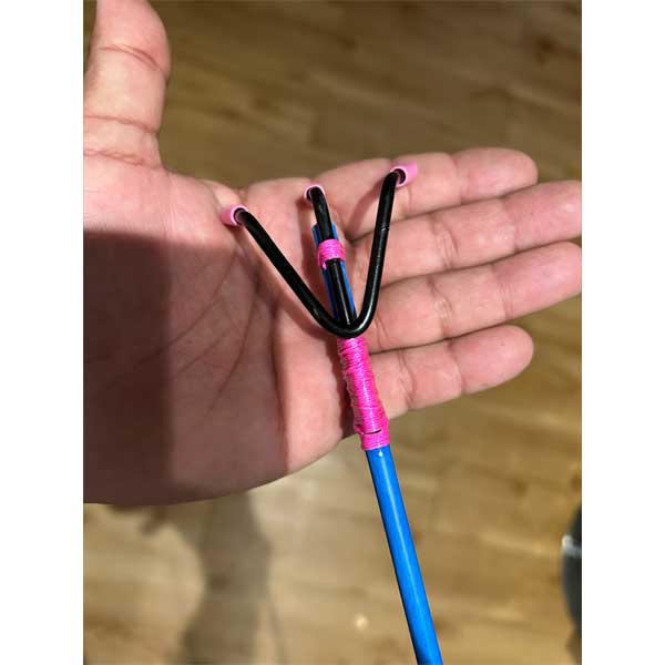 Hand holding a blue and pink slingshot against a wooden background