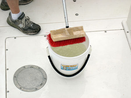Bucket with a scrub brush and cleaning solution on a white floor.