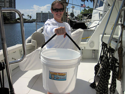 Person holding a white bucket on a boat with water and buildings in the background
