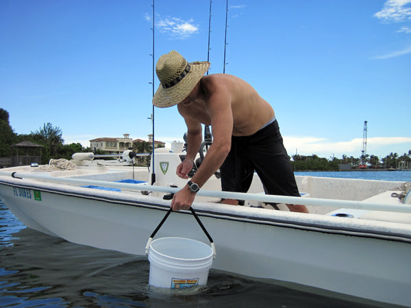 Man on a boat holding a bucket, with fishing equipment and a clear sky in the background.