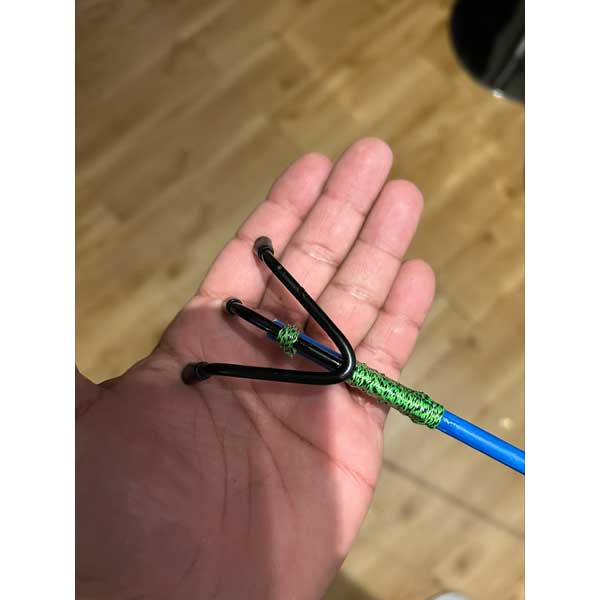 Hand holding a bow with green string and blue shaft on a wooden floor background
