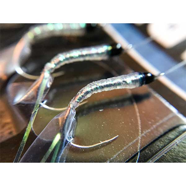 Close-up of fishing hooks with worms on a reflective surface